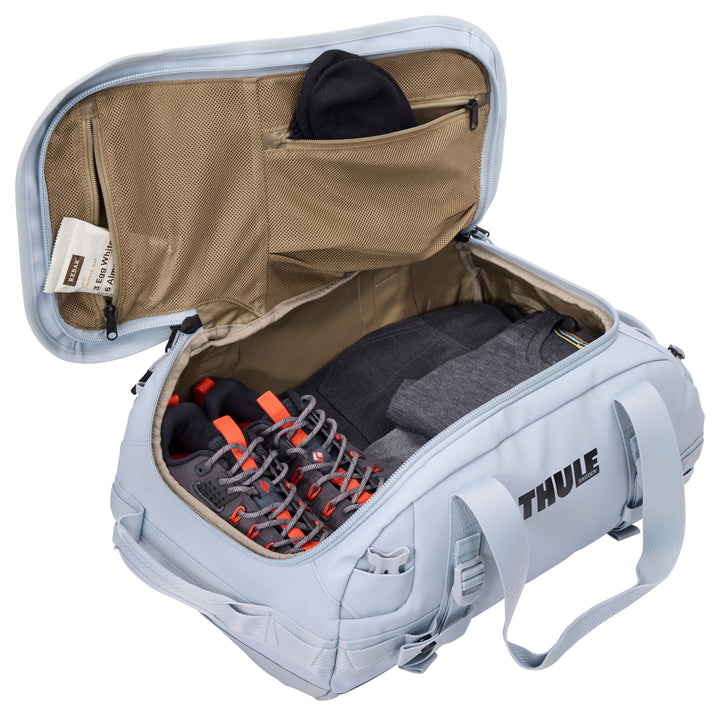 Gray Thule backpack with open lid showing a shoe and clothing inside on a white background