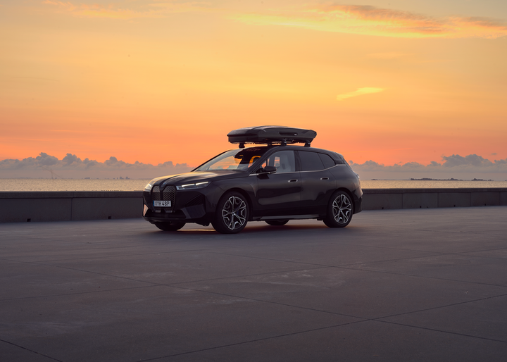 Black SUV parked near a waterfront with Thule Motion 3 XL Low rooftop cargo box at sunset background.