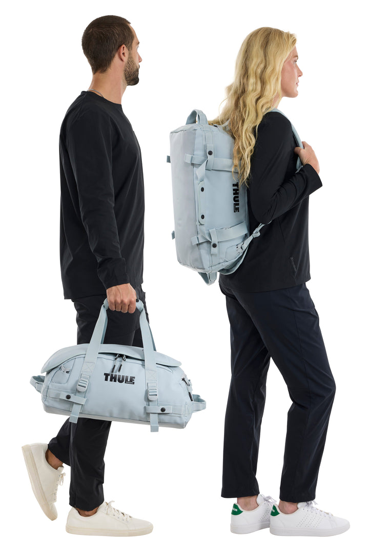 Two people carrying Thule bags, one duffel and one backpack, on a white background.
