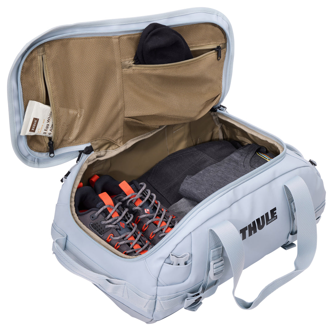 Gray Thule backpack with open lid showing a shoe and clothing inside on a white background